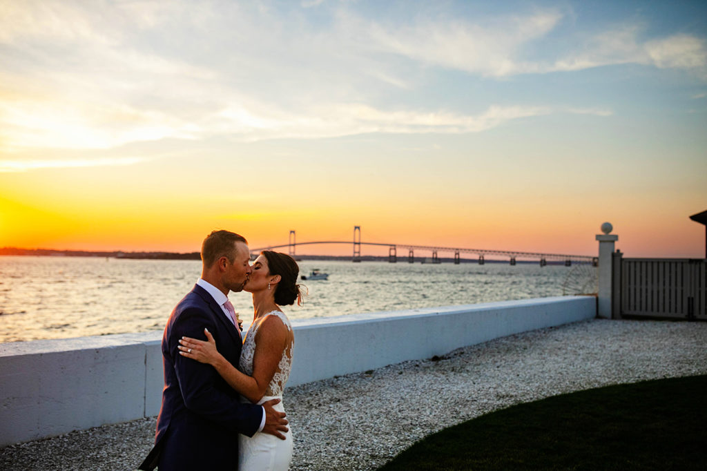 Bride and groom kissing at sunset with the newport bridge behind them at Belle Mer