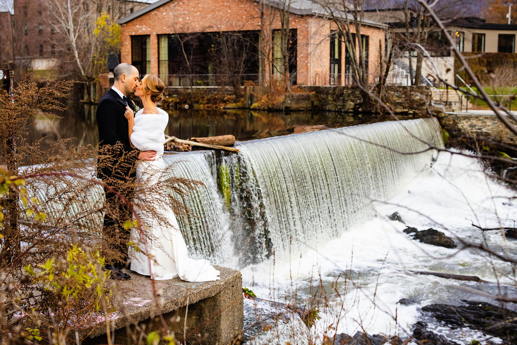 Bride and groom kissing by the waterfall next to their wedding venue, the Roundhouse, in Beacon NY