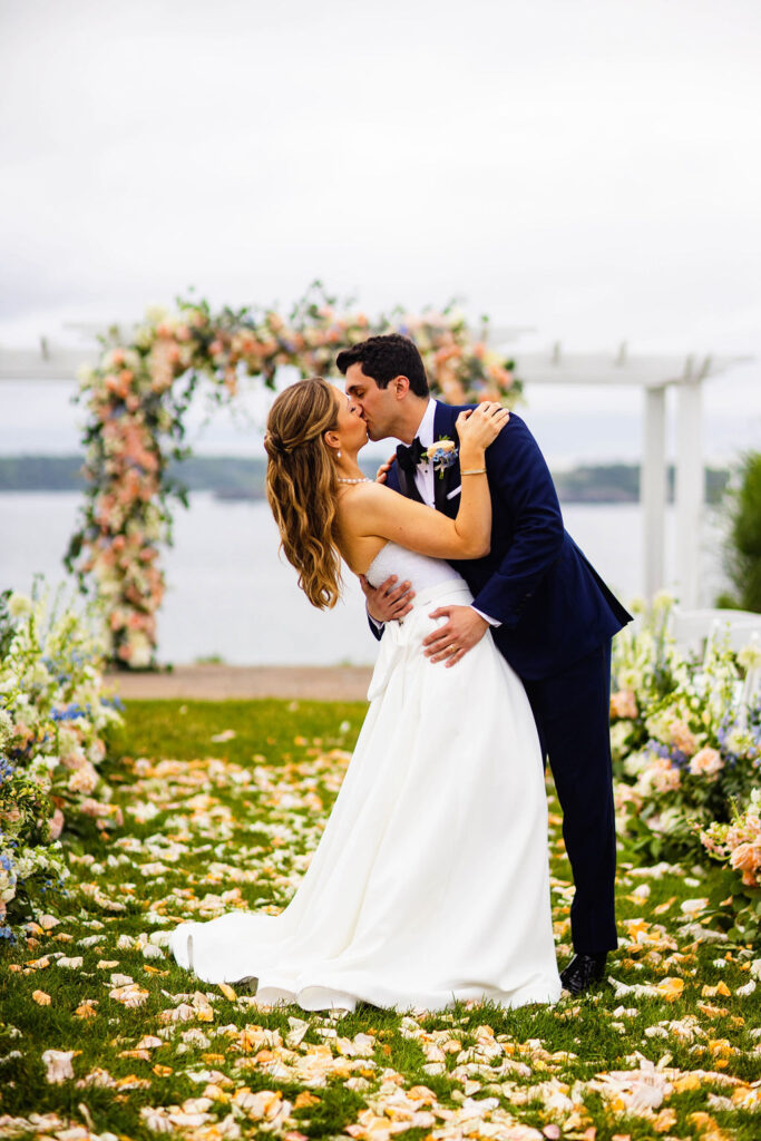 Bride and groom kissing by their ceremony site that is covered in florwers at their Oceancliff wedding in Newport, RI