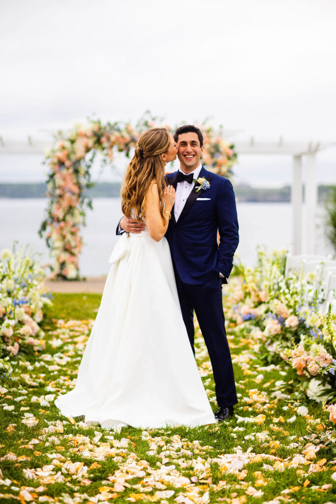 Bride and groom kissing by their ceremony site that is covered in florwers at their Oceancliff wedding in Newport, RI