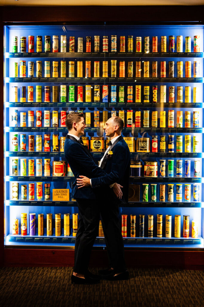 Grooms standing in front of tennis bass display at their wedding held at the Tennis Hall of Fame in Newport, RI