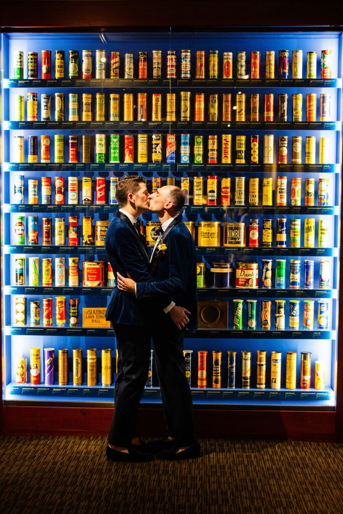 Grooms standing in front of tennis bass display at their wedding held at the Tennis Hall of Fame in Newport, RI