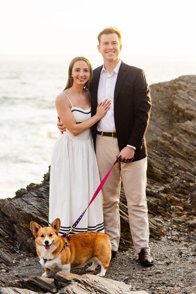 An engaged couple pose with their corgi at their Beavertail engagement session in Jamestown