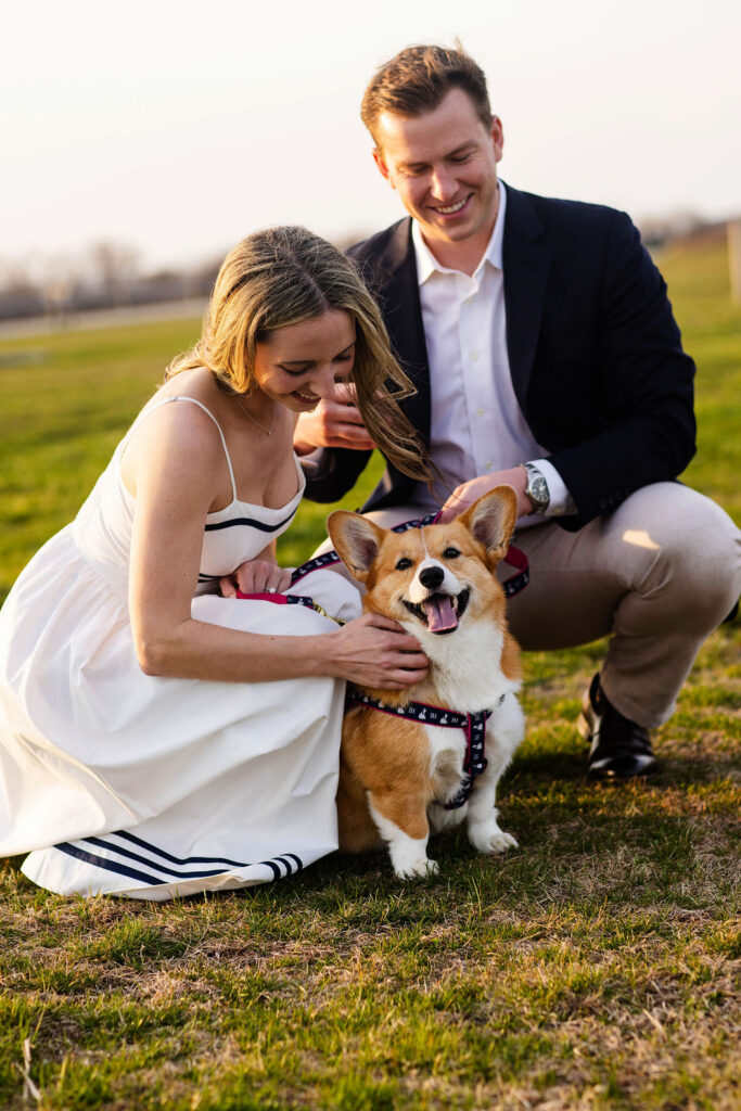 An engaged couple squat down with their corgi at their Beavertail engagement session in Jamestown